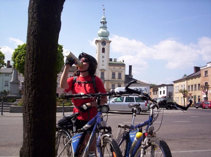 Rowerzystka pijąca z bidonu na tle zabytkowego placu z wieżą zegarową