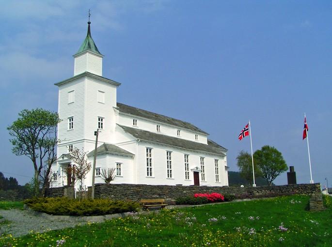 Biała drewniana kaplica na wzgórzu z flagami Norwegii