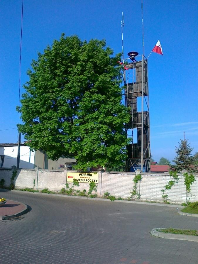 Za płotem wieża i budynek Straży Pożarnej