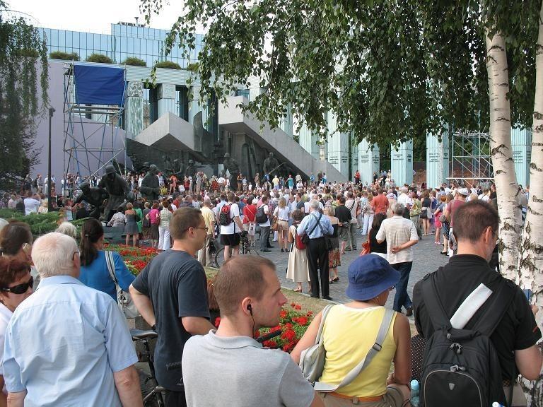 ruch przed pomnikiem- ludzie składają kwiaty, zapalają znicze. 3 minuty do 17tej