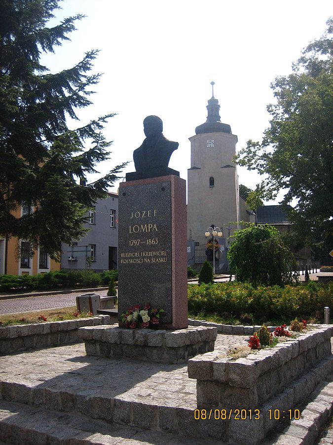 Kościół pod wezwaniem Świętej Katarzyny w Woźnikach. Na pierwszym planie upamiętnienie Józefa Lompy - śląskiego działacza i poety, pochowanego na miejscowym cmentarzu