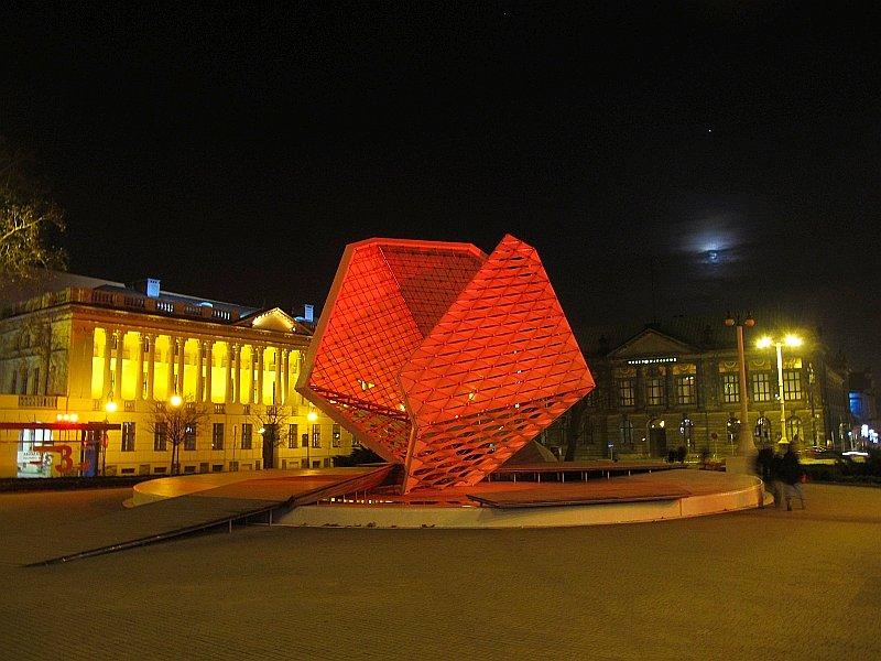 Plac Wolności. Na lewo Bibloteka Raczyńskich, w środku iluminowana gontanna, na prawo Muzeum Narodowe,a u góry świecący Księzyc