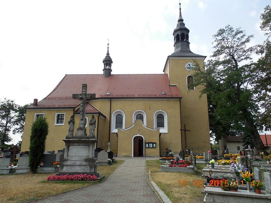 Sic enim Deus dilexit mundum, ut Filium suum unigenitum daret - Tak bowiem Bóg umiłował świat, że Syna swego Jednorodzonego dał – głosi cytat z Ewangelii wg Świętego Jana na cokole krzyża przed Kościołem w Kotach