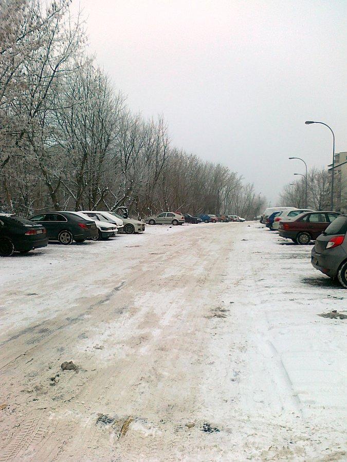 Boczna uliczka osiedlowa pokryta ubitym śniegiem i lodem
