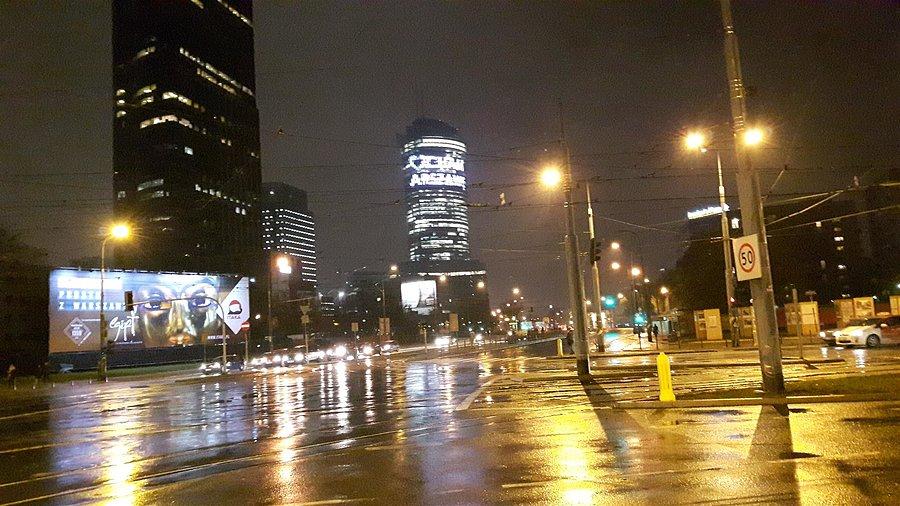 Skrzyżowanie na Woli z widokiem na wieżowce w wieczornym deszczu
