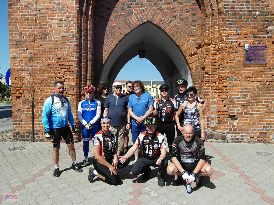 Grupa rowerzystów pod ceglaną bramą