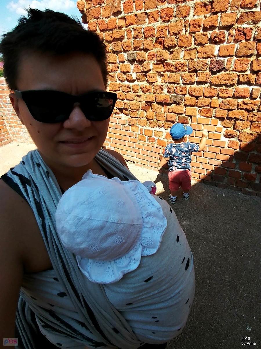Mama z niemowlakiem w chuście na tle ceglanej ściany