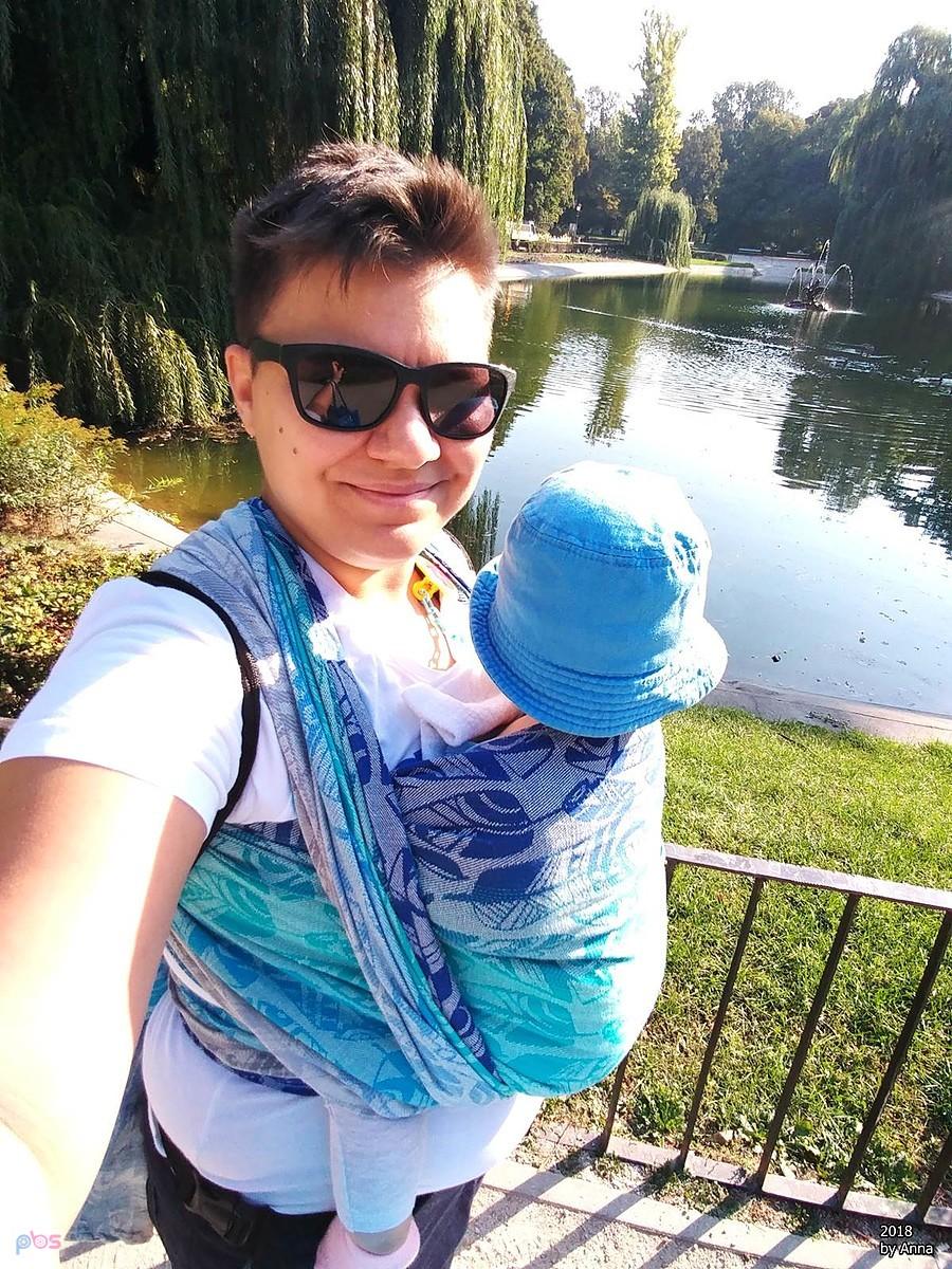 Mama z dzieckiem w nosidełku na spacerze w parku