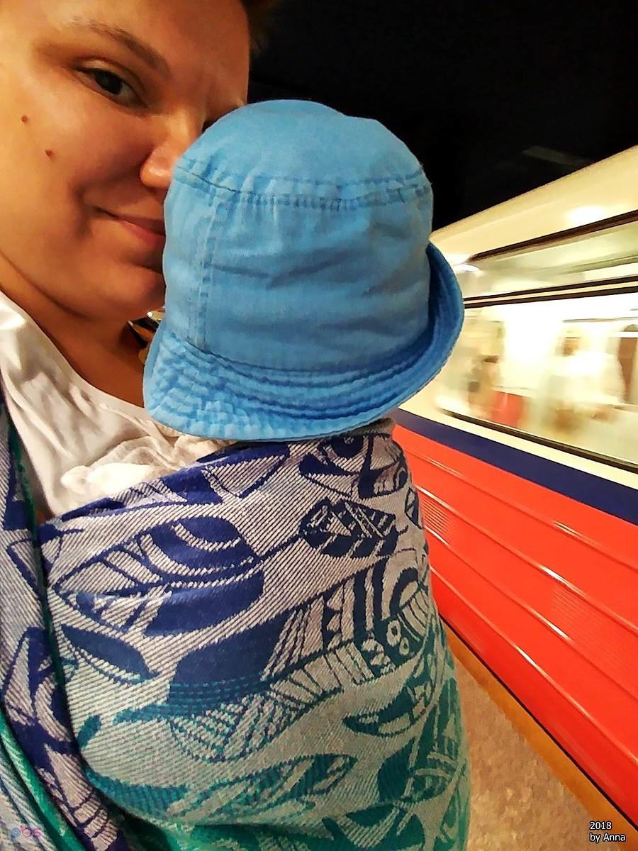 Kobieta z niemowlakiem w nosidełku na stacji metra