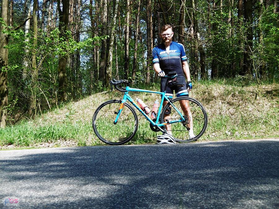 Rowerzysta z turkusowym rowerem na leśnej drodze