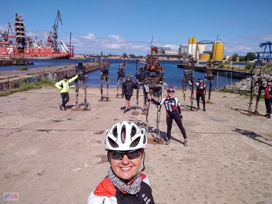 Rowerzystka w kasku robi selfie na tle portu stoczniowego