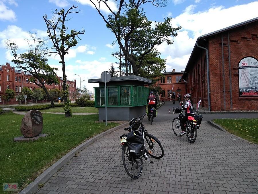 Rowerzyści na ścieżce przy ceglanej zabudowie