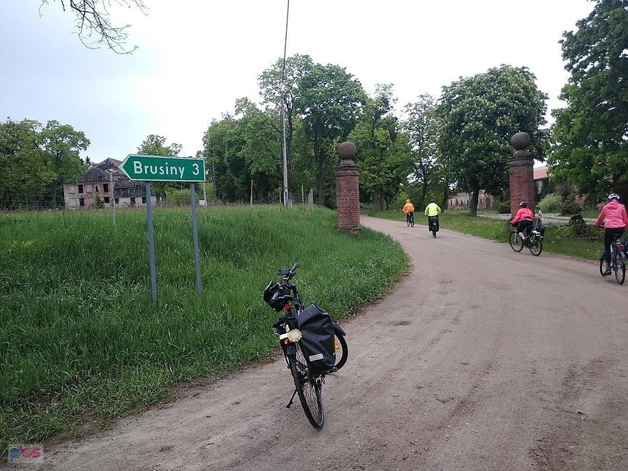 Rowerzyści na wiejskiej drodze przy bramie z kolumnami