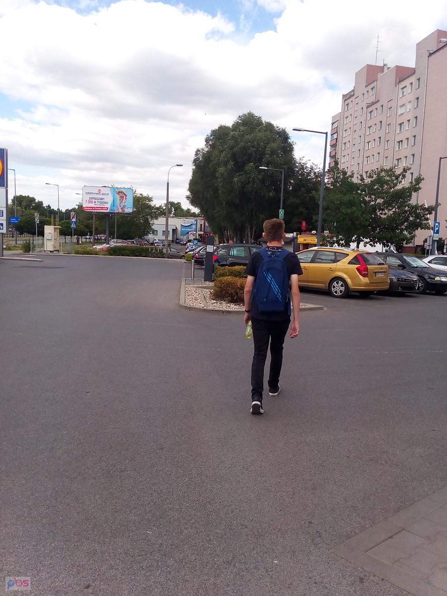 Mężczyzna z plecakiem idzie po parkingu miejskim