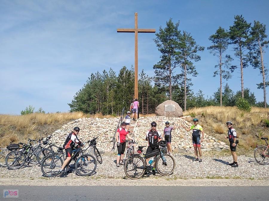 Grupa rowerzystów na szlaku przy krzyżu