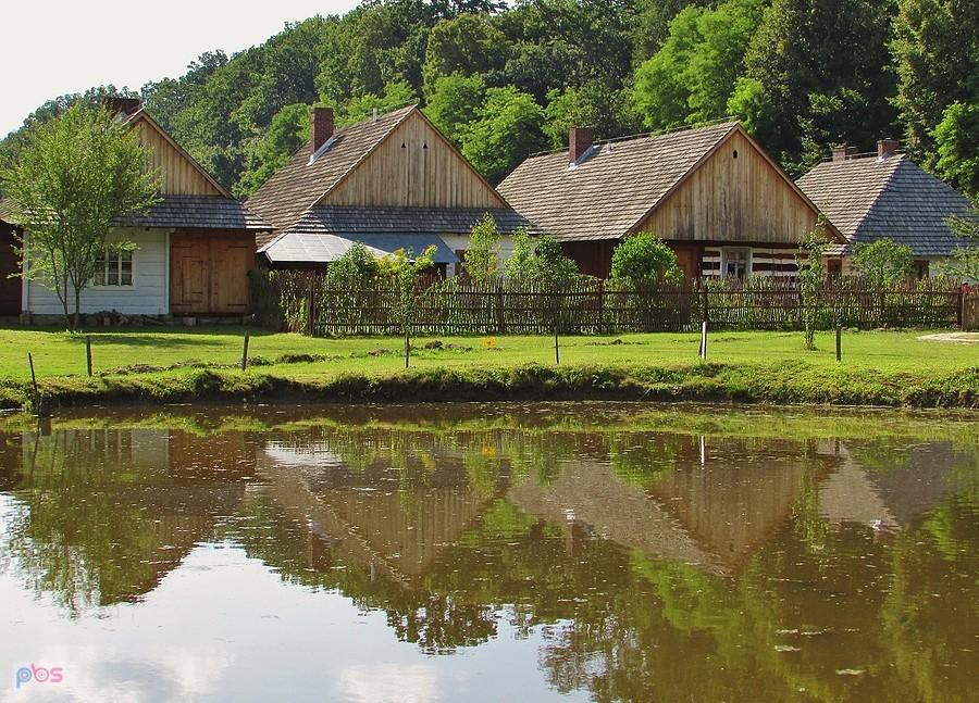 Skansen w Sanoku - chaty z Jaślisk stojące przy Rynku Galicyjskim przeglądają się w stawie
