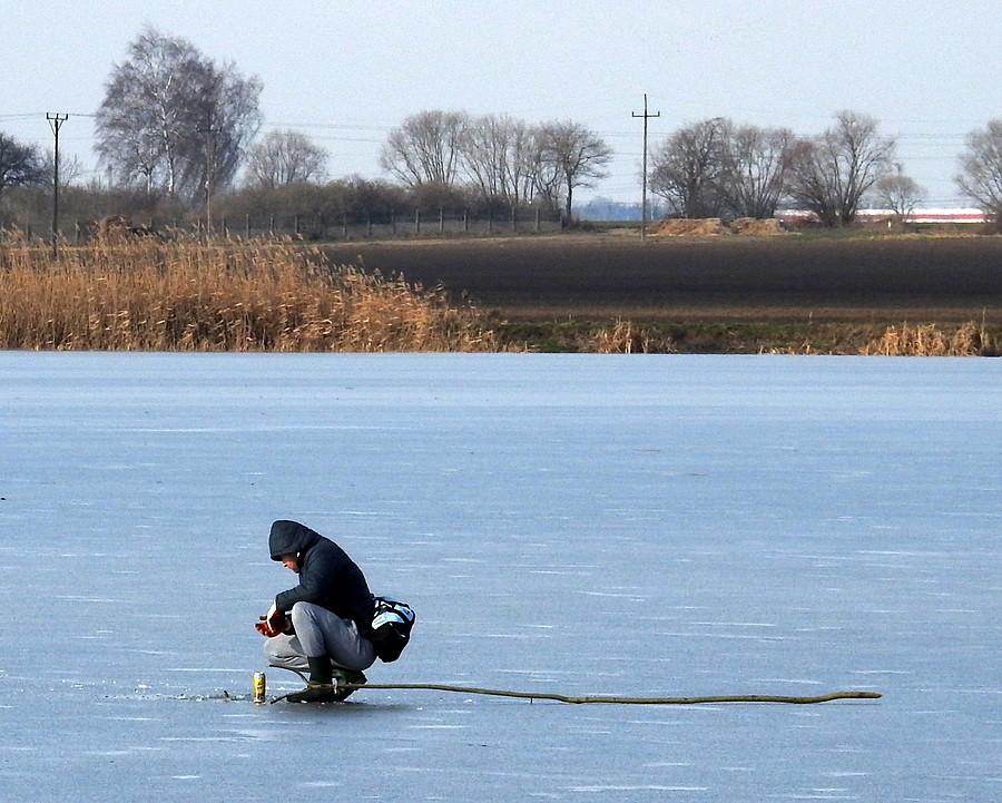 Dziwny spacerowicz na lodzie, z kijem obok i browarem w ręku