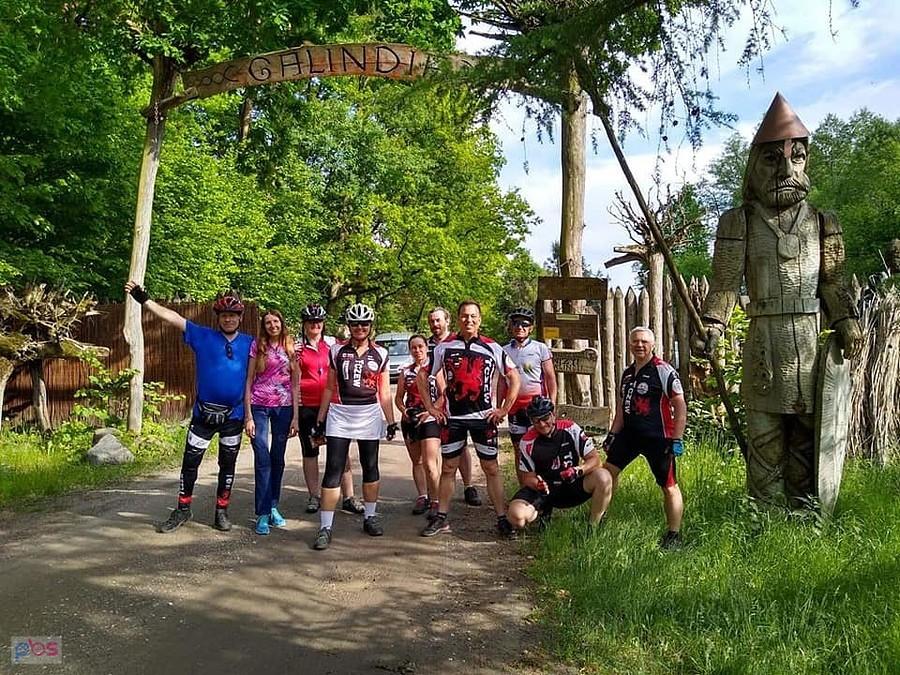 Grupa rowerzystów przed wejściem do parku z drewnianą bramą