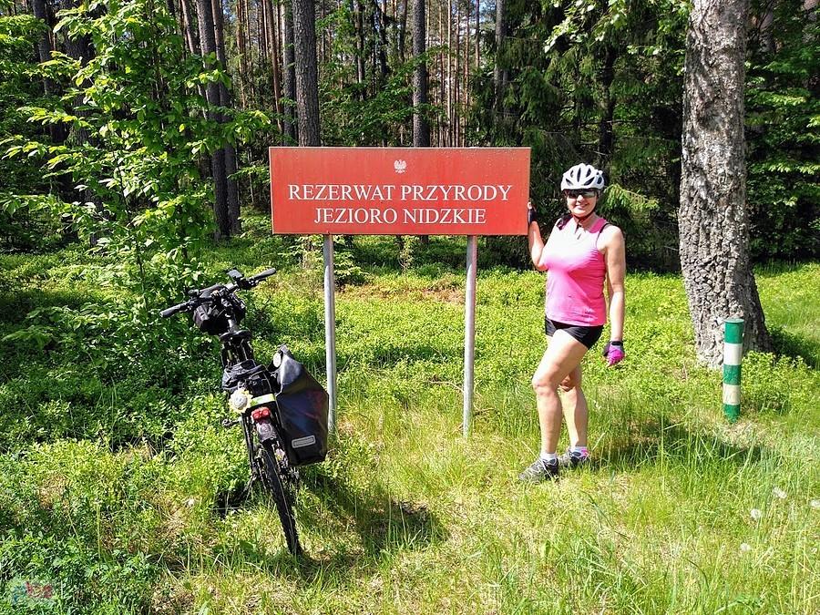 Rowerzystka przy tablicy rezerwatu Jezioro Nidzkie
