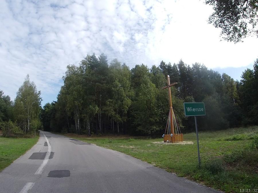 Drewniany krzyż przy drodze obok znaku miejscowości