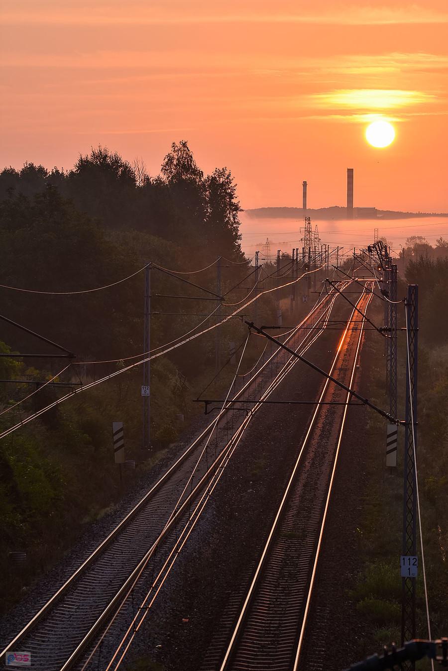 Wschód słońca nad linią kolejową D29-61 w Częstochowie. Na horyzoncie kominy huty szkła "Guardian".