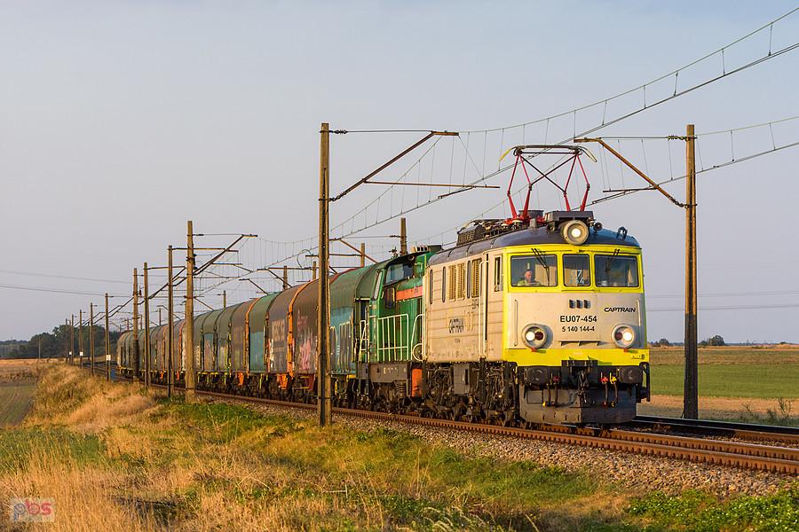 EU07-454 wraz z "zimną" SM42-2486 i składem krytych wagonów jadą szlakiem linii D29-152: Czarków -> Toszek Północ mijając wieś Świbie.