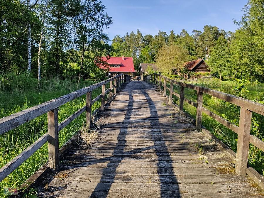 Drewniany długi most nad mokradłami prowadzi do leśniczówki
